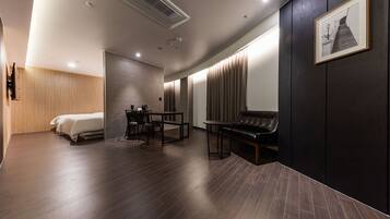 A modern hotel room with a bed, a desk, a chair, a sofa, and a large window with curtains.