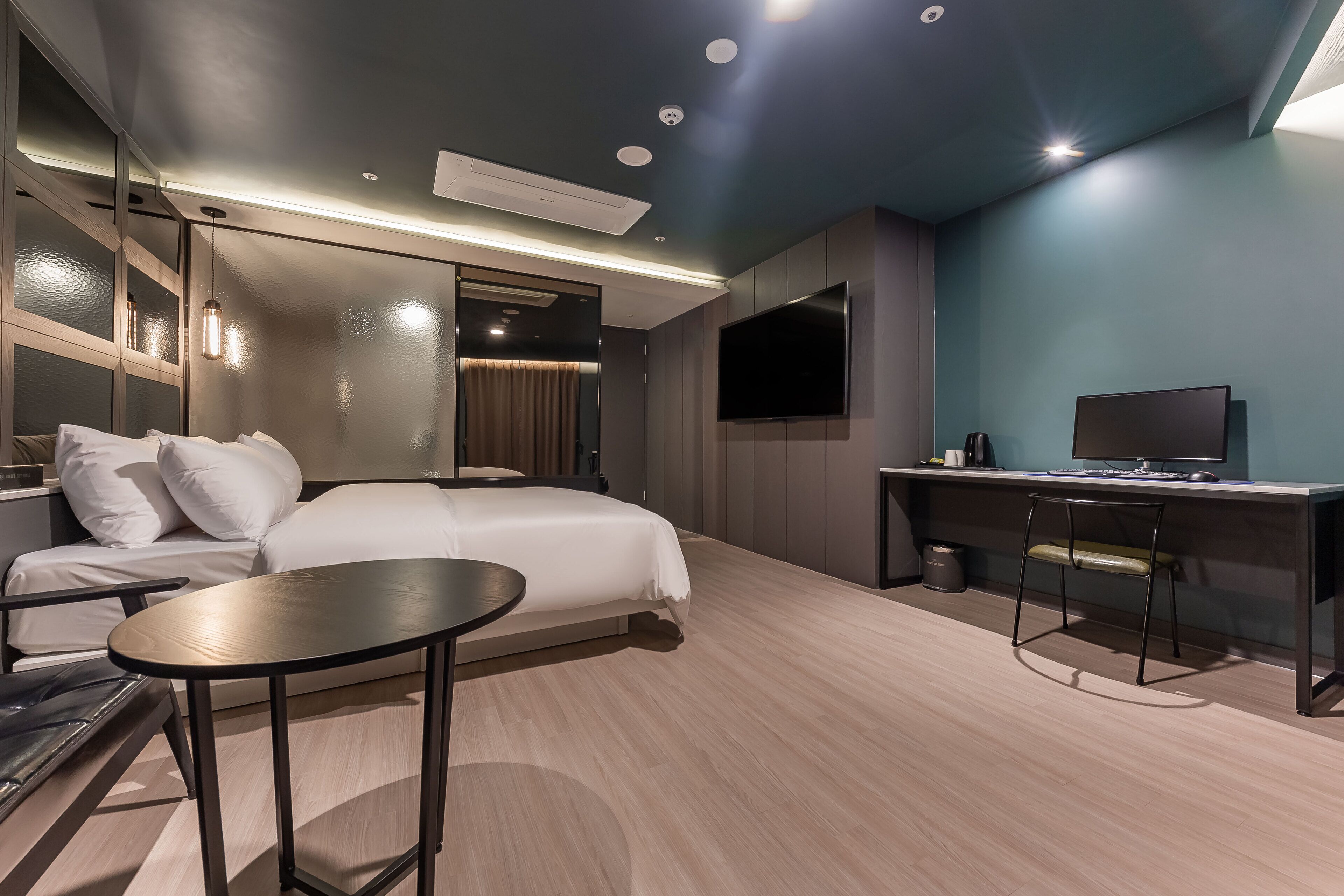 A modern hotel room with a bed, a desk, a chair, a TV, and a mirror.
