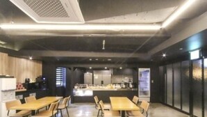 A modern dining area with wooden tables and chairs, a central island with kitchen appliances, and a dark-toned interior. - Seosan Browndot Hotel (Seosan)