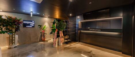A modern reception area with a marble floor, potted plants, a flat-screen TV, and a 'Welcome' sign.