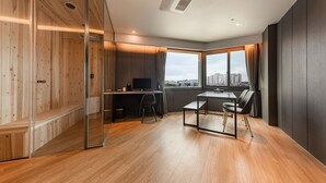 A modern room with a wooden floor, a glass partition, a desk with a computer, a dining table with chairs, and a large window offering a city view. - Seosan Browndot Hotel (Seosan)