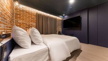 Quarto de hotel moderno com parede de tijolos decorativa, uma TV de tela plana fixada na parede e uma cama com roupa de cama branca.