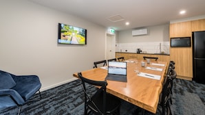 A conference room with a wooden table, black chairs, a laptop, and a television on the wall. - Avenue Motel Apartments (South Toowoomba)