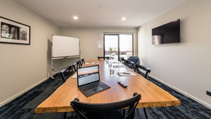 A conference room with a long wooden table, black chairs, a laptop, a whiteboard, and a TV on the wall. - Avenue Motel Apartments (South Toowoomba)