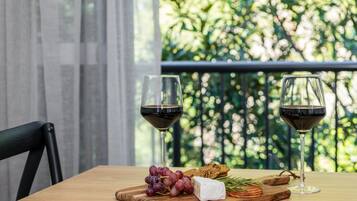 A table with a wooden cutting board, a glass of red wine, a piece of cheese, and a bunch of grapes.