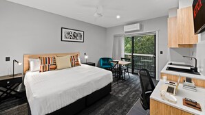 A modern hotel room with a large bed, a desk with a laptop, a chair, and a view of the outdoors. - Avenue Motel Apartments (South Toowoomba)