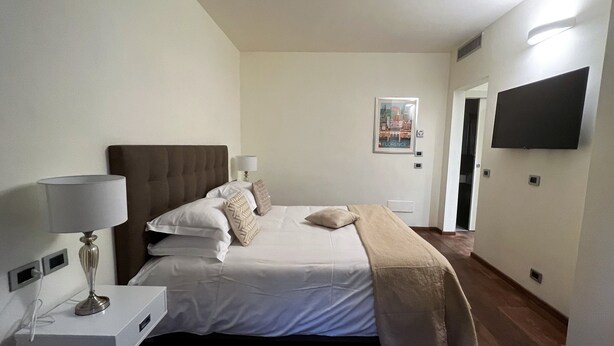 Ein Hotelzimmer mit Bett, Nachttischlampen, einem an der Wand befestigten Flachbildfernseher und einem Bilderrahmen mit einem Florentiner Stadtbild.