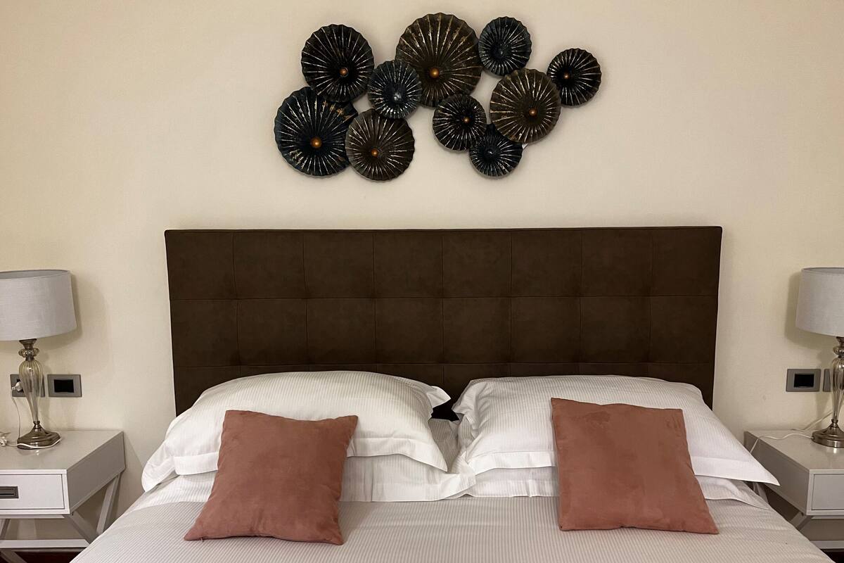 A hotel room with a large bed, two nightstands, a wall-mounted decorative piece, and two lamps.