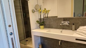 Ein modernes Badezimmer mit Waschbecken, Spiegel, einer Orchidee im Topf und einer Duschkabine aus Glas.