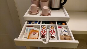Ein Tablett mit zwei rosafarbenen Tassen und einer silbernen Kaffeekanne, darunter eine Schublade mit Kaffeekapseln und Teebeuteln.