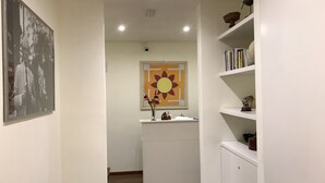 Ein Flur mit weißer Wand, einem gerahmten Bild, einer Blumenvase, einem sonnenförmigen Kunstwerk und einem weißen Schrank.