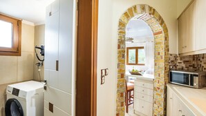 Un área de lavandería con lavadora y secadora, una cocina con microondas y un arco que conduce a un comedor.