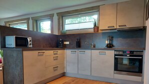 A modern kitchen with built-in appliances, wooden flooring, and large windows.