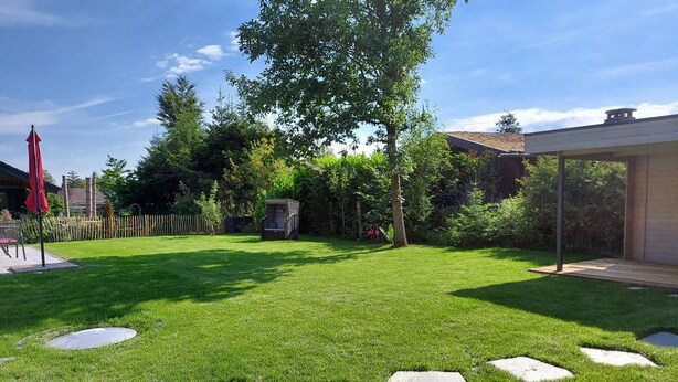 A well-maintained backyard with a grassy lawn, a wooden deck, and a covered seating area.