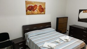 Une chambre à coucher avec un lit, une table de chevet, une commode, une chaise et un tableau au mur.