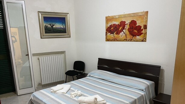 Une chambre à coucher avec un lit, une chaise, un radiateur et deux tableaux accrochés au mur.