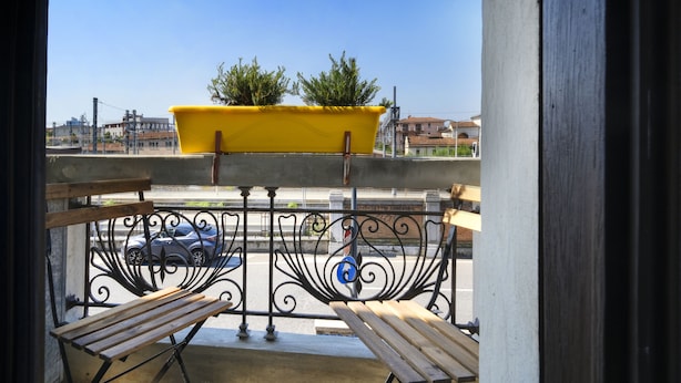 A balcony with a yellow planter, two benches, and a view of the street and buildings. - albinariobrescia  (Brescia)