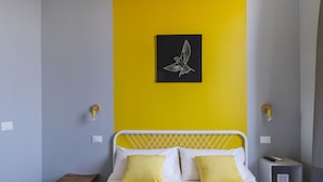 A bedroom with a bed, two yellow pillows, a white headboard, a small wooden stool, and a nightstand with a lamp. - albinariobrescia  (Brescia)