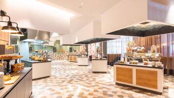 Eine moderne Hotellobby mit einem geometrisch gemusterten Boden, einer zentralen Insellounge mit Glastisch und einem Wandgemälde mit Bergmotiven.