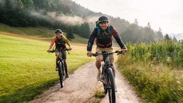 Zwei Radfahrer auf einem asphaltierten Weg, umgeben von Grün und Hügeln.