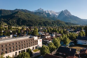 A residential area with a modern building featuring a logo, surrounded by houses and trees, with mountains in the background.