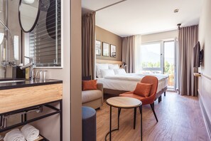 A hotel room with a bed, a sofa, a round table, a TV, and a bathroom with a mirror and sink.