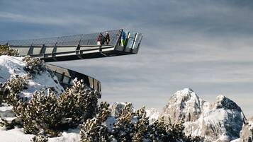Montaña nevada con un puente peatonal y cumbres rocosas al fondo.