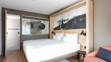 A bedroom with a large bed, a wooden headboard, a painting of a mountain, and a small side table.