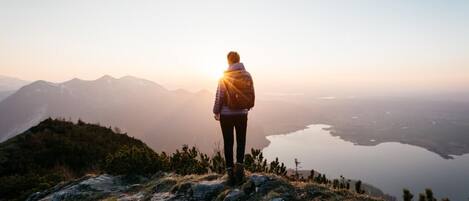 Une personne se tient debout sur un promontoire rocheux, d’où elle a une vue sur un lac et des montagnes.