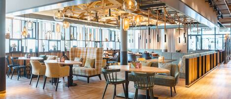 A modern restaurant with wooden floors, multiple seating areas including tables and booths, and hanging pendant lights.