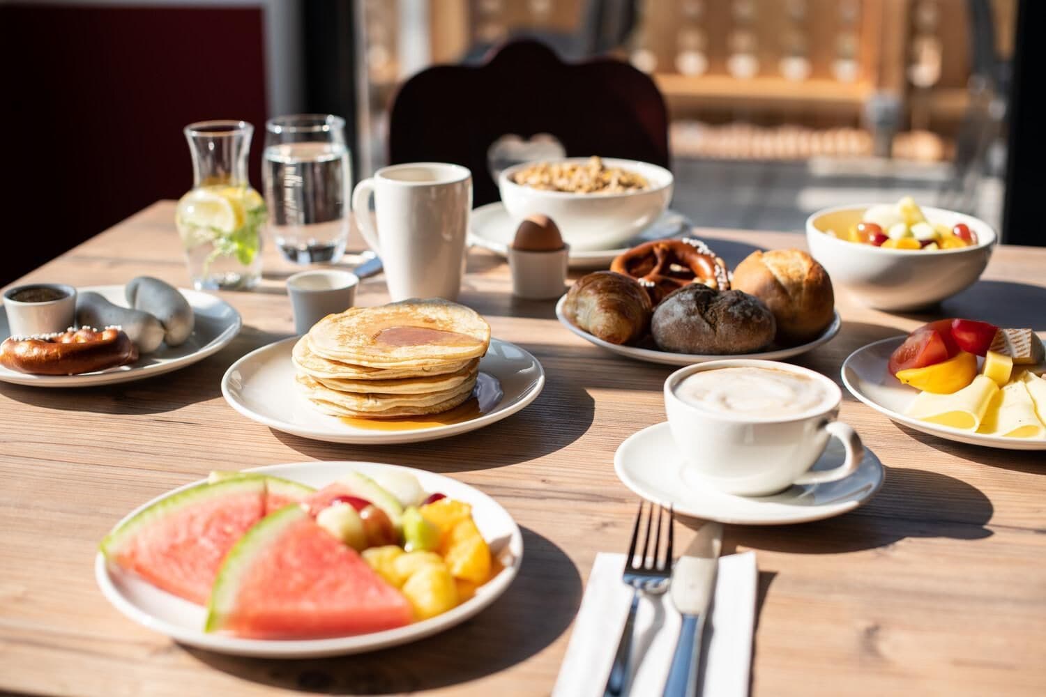 Una tavola per la colazione con diversi piatti, tra cui pancakes, croissant e frutta.