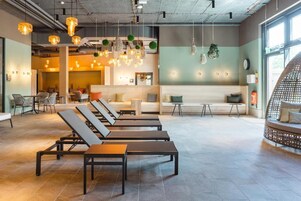 Un espace de détente moderne avec des chaises longues, un comptoir d’accueil et des luminaires suspendus.