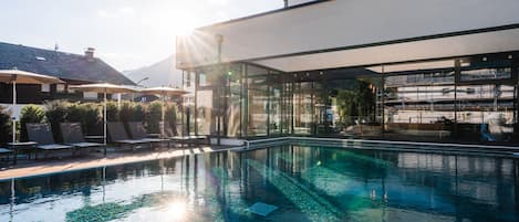 Un área de piscina moderna con agua cristalina, un entorno bañado por el sol y una vista de la montaña al fondo.