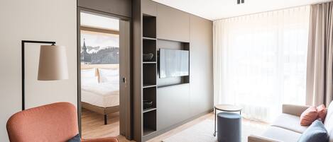 A modern hotel room with a bed, a sofa, a TV mounted on the wall, and a view of a mountain through the window.