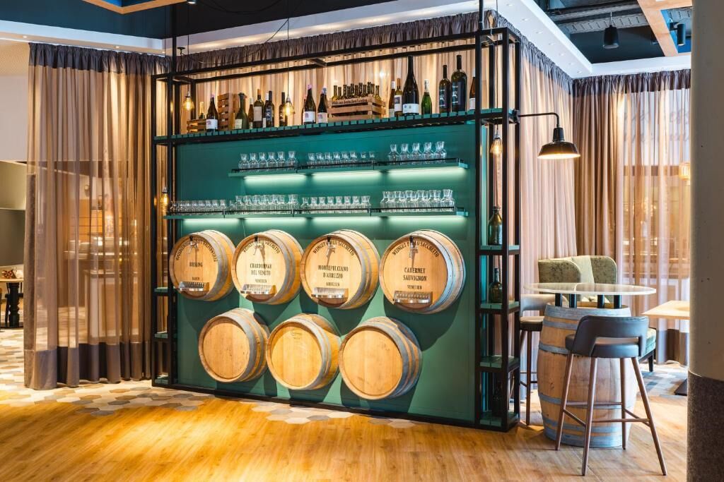 A bar area with wooden barrels, shelves of bottles, and a seating area with a round table and chairs.