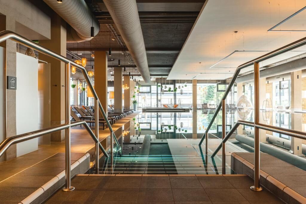 Un interior moderno con una escalera de cristal, barandillas de metal y una zona de estar con vistas al exterior.
