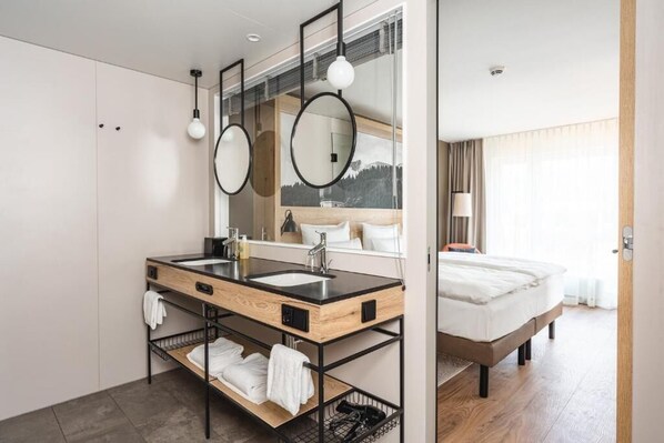 Habitación de hotel moderna con tocador doble, espejo grande, cama y vista al exterior.