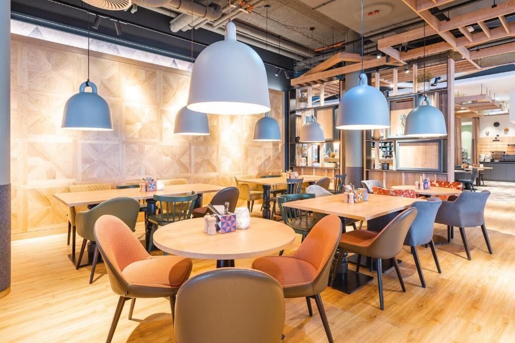 Interior moderno de restaurante con mesas redondas, sillas e iluminación colgante.