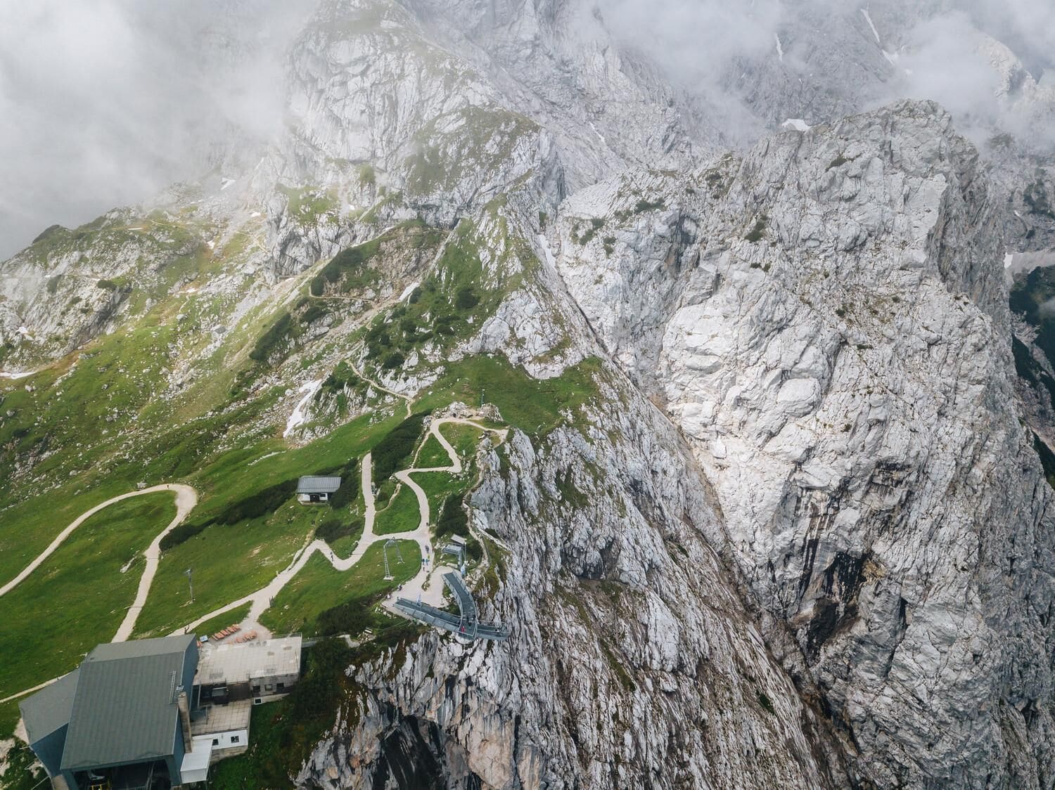 Een bergachtig landschap met een kronkelend pad, een klein gebouw en een brug.