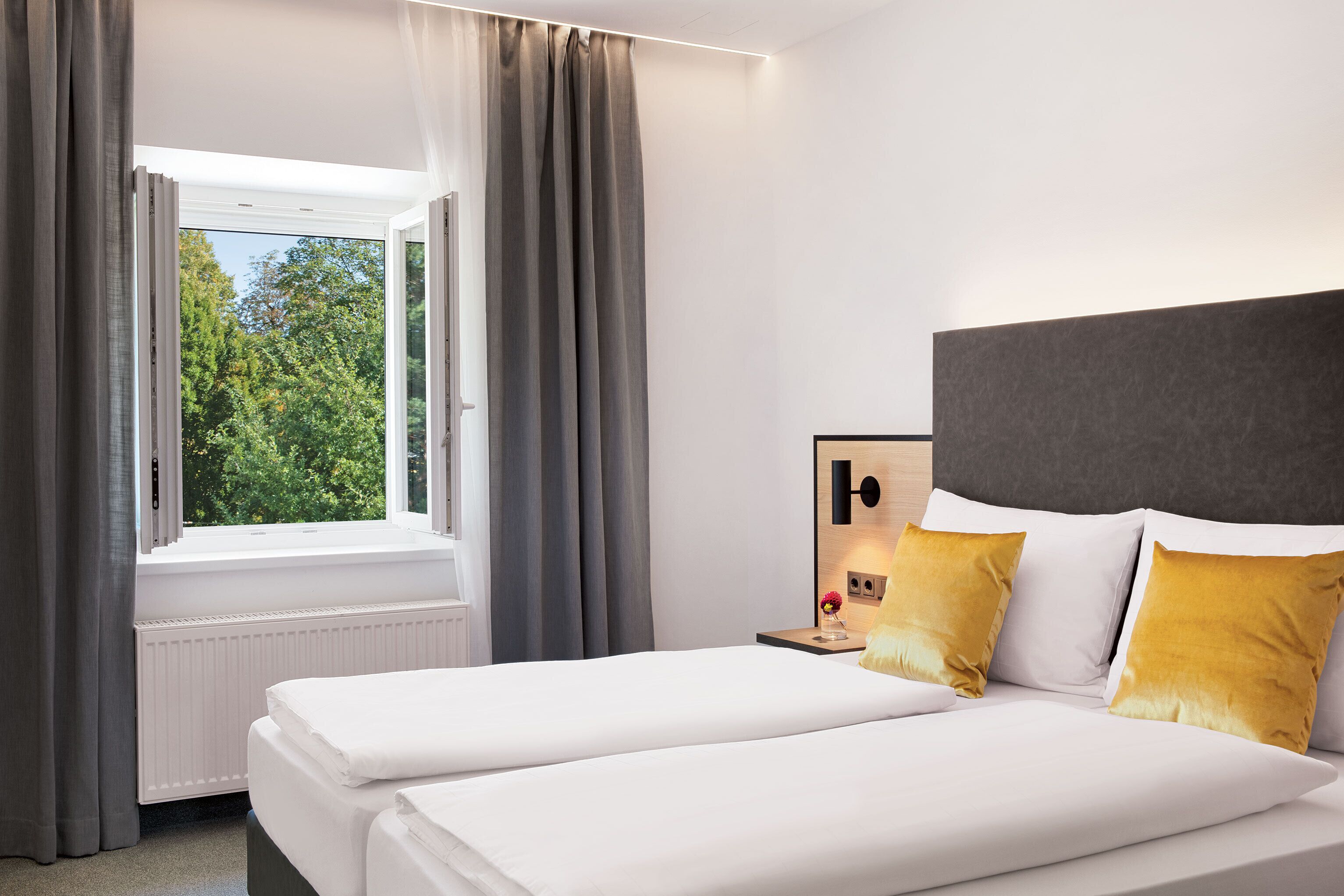 Een hotelkamer met een groot raam, een bed met wit beddengoed en een nachtkastje met een lamp.