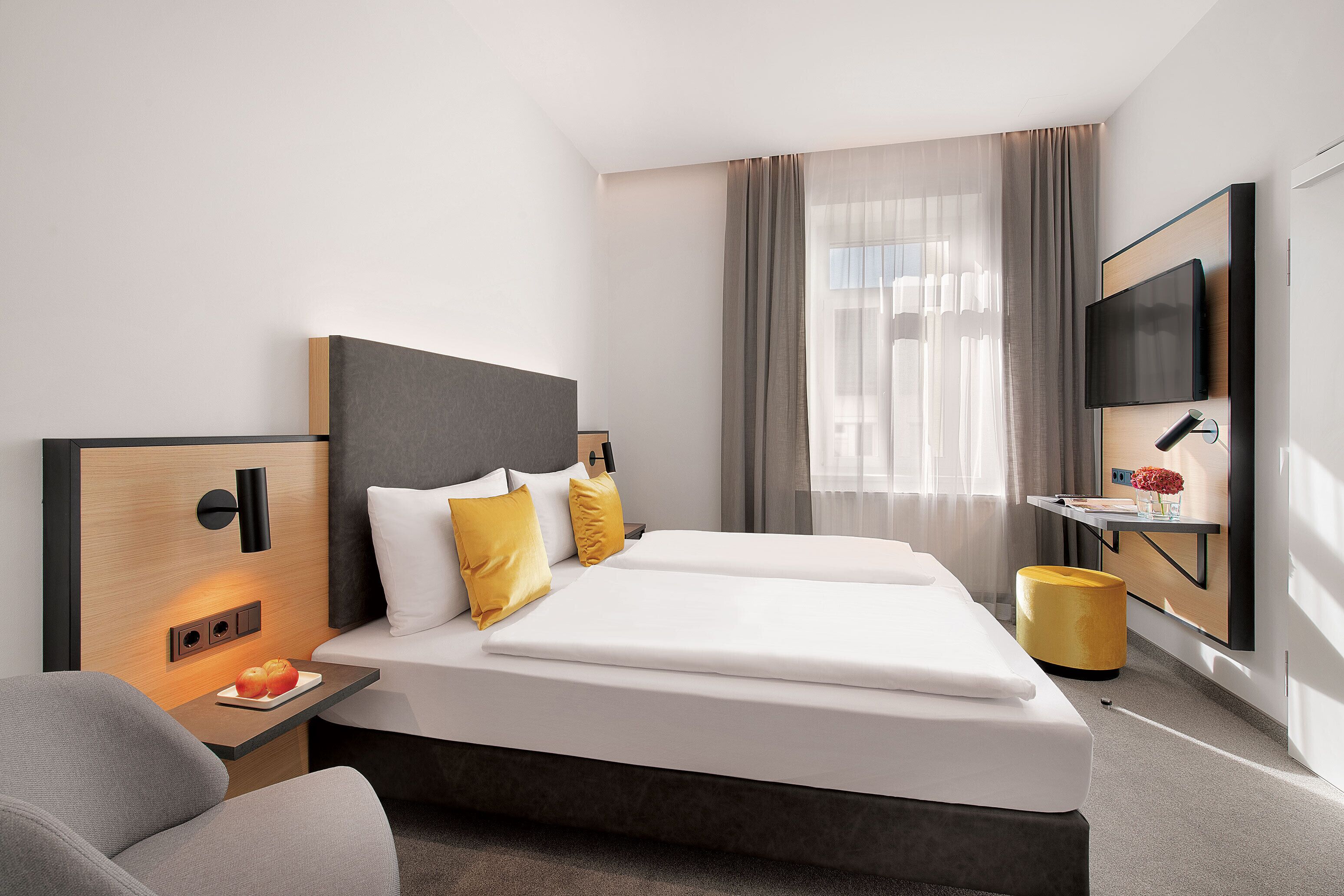Habitación de hotel moderna con una cama grande, mesitas de noche, un televisor de pantalla plana y una pequeña zona de escritorio.