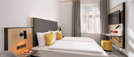 Habitación de hotel moderna con una cama grande, mesitas de noche, un televisor de pantalla plana y una pequeña zona de escritorio.