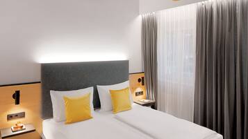 Quarto de hotel moderno com uma cama grande, vigas de madeira, mesa de cabeceira e uma janela com cortinas.