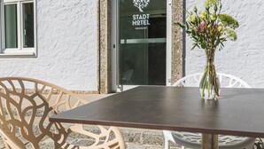 A hotel entrance with a sign reading "Stadt Hotel," outdoor seating with chairs, and a vase with flowers on the table. - Stadthotel Oberndorf - 24h Self Check-In Terminal  (Oberndorf bei Salzburg)