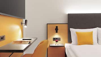 A hotel room with a bed, a desk, a chair, and a nightstand with a lamp.