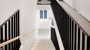 A modern staircase with wooden beams, a black railing, and a light fixture. - Stadthotel Oberndorf - 24h Self Check-In Terminal  (Oberndorf bei Salzburg)
