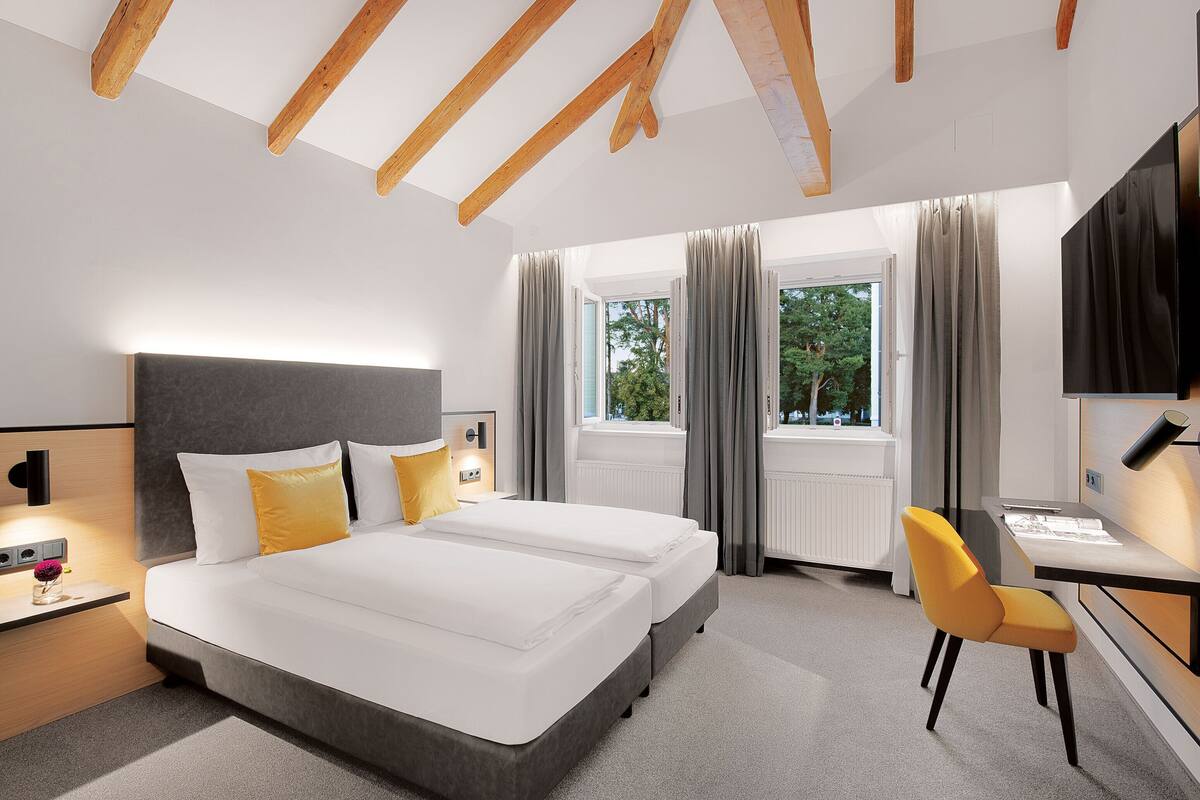 Ett modernt hotellrum med en stor säng, ett skrivbord och en stol. Det finns ett fönster med gardiner, en tv och en lampa på nattduksbordet.