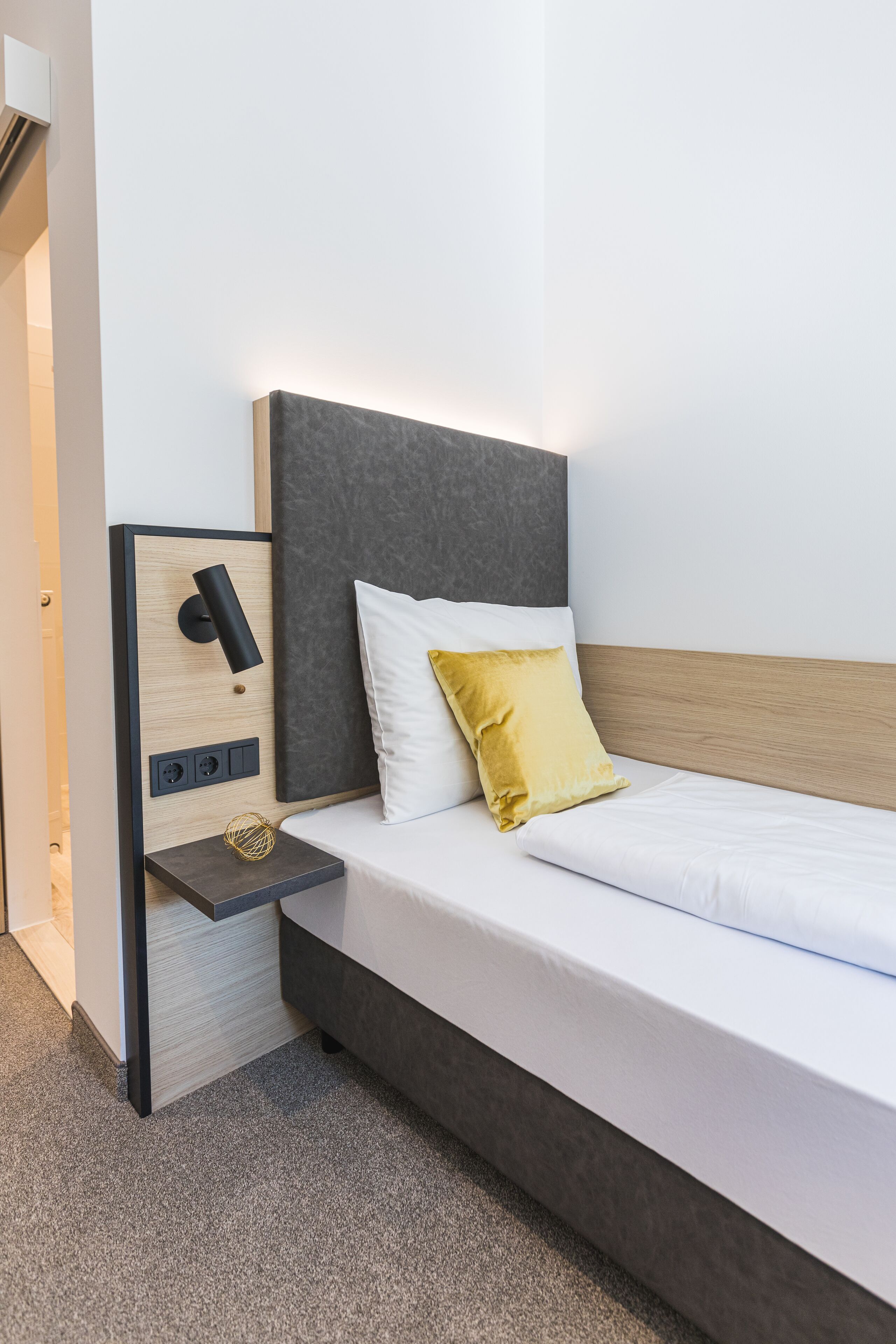 Une chambre d’hôtel moderne équipée d’un lit, d’une table de chevet et d’un luminaire fixé au mur.