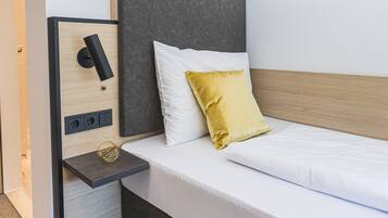 Une chambre d’hôtel moderne équipée d’un lit, d’une table de chevet et d’un luminaire fixé au mur.