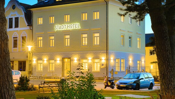 A hotel with a sign reading "STAHL HOTEL" at night, surrounded by trees and a well-maintained lawn. - Stadthotel Oberndorf - 24h Self Check-In Terminal  (Oberndorf bei Salzburg)